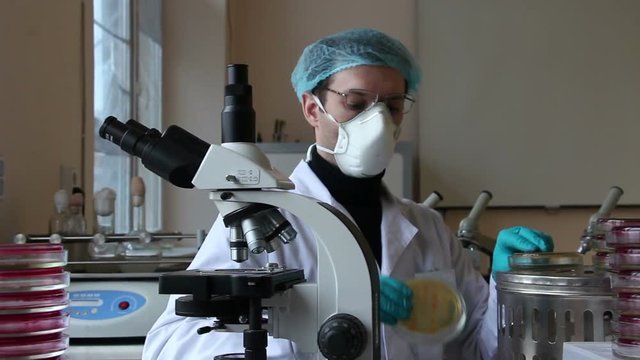 Researcher observes the petri dishes in bacteriological science laboratory. Moving equipments background. Bacterial cultures are in petri plates. Panning dolly slider shot.