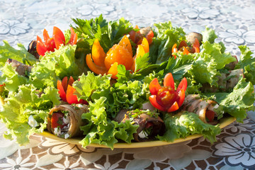 Rolls from eggplant and lettuce leaves decorated with flowers cut from cherry tomatoes on a white tablecloth side view