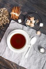 Cup of black tea on wooden table with cane and white sugar cubes, tea spoon and tea strainer. Top view.