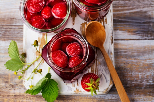 Homemade strawberry jam with whole berries in glass jars on wooden table. Toned image. Copy space