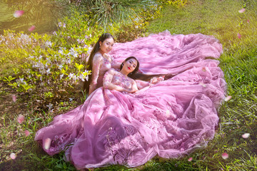 Beautiful happy two sisters in pink dresses, lie near blooming sakura(cherry)