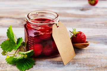 Homemade strawberry jam with whole berries in glass jars on wooden table. Toned image. Copy space