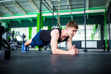 Fototapeta na wymiar Young man workout in fitness club. Profile portrait of caucasian guy making plank or push ups exercise, training indoors