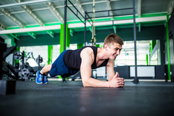 Obraz na płótnie Canvas Confident muscled young man wearing sport wear and doing plank position while exercising on the gym interior
