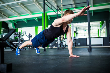 Confident muscled young man wearing sport wear and doing plank position while exercising on the gym interior