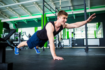 Fototapeta na wymiar Confident muscled young man wearing sport wear and doing plank position while exercising on the gym interior