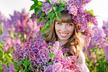 The beautiful young woman with a lilac wreath on her head holds a lilac bouquet