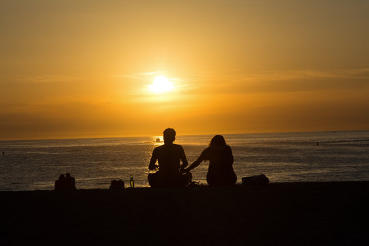 Silhouette of a couple sitting on the beach, watching the sunset