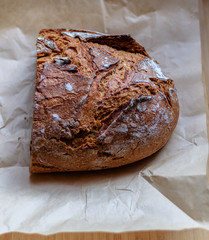 A fresh, crunchy, delicious rye bread on a wrinkled paper and a wooden chopping board