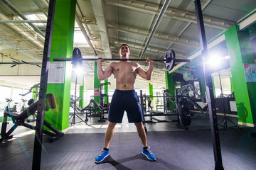 Fit young man lifting barbells looking focused, working out in a gym