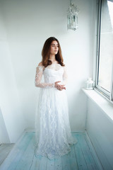 The bride on a white background in a white lace dress. Beautiful natural beauty. Light makeup and loose hair. Natural.