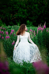 Obraz na płótnie Canvas Beautiful bride in bright lace dress. In a field with Ivan-tea. Natural beauty, minimal makeup and loose hair. A child of nature