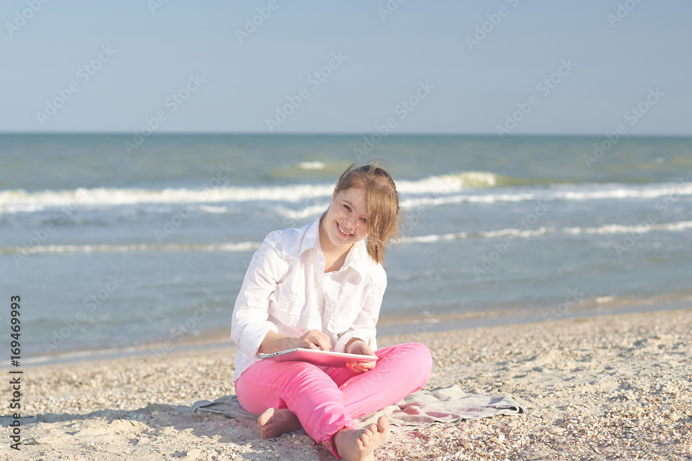 Wall mural Girl seventeen-year-old  with Down syndrome on the beach play with the tablet.