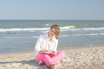 Fototapeta na wymiar Girl seventeen-year-old with Down syndrome on the beach play with the tablet.