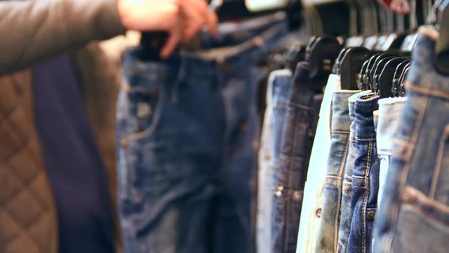 Male customer in fashion store choosing jeans. Person in shopping mall. Sales concept. 4K UHD video footage. Ultra high definition 3840X2160