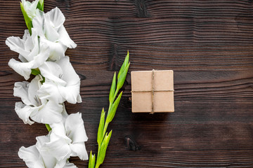 To wrap a gift. Box in kraft paper near flower gladiolus on dark wooden table top view copyspace