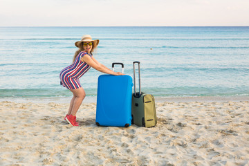 Happy laughing woman tourist with suitcases standing near the sea. Travel and summer vacation concepts