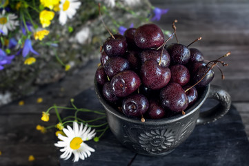Ripe juicy cherries in a clay pot with field daisies and bells in a rustic style.