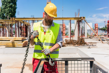 Reliable young worker checking the safety latch of a hook before lifting heavy weight with the crane on the construction site