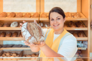 Saleslady in bakery shop presenting bread to potential buyer