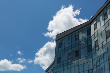 fragment of a glass building against a blue sky with a big cloud