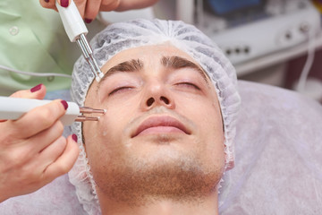 Microcurrent face therapy close up. Young man, cosmetology procedure.