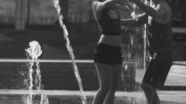 Young happy couple dancing in the fountain