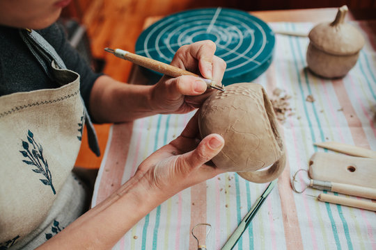 Woman potter making pattern on the ceramic cup in her workshop