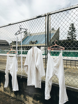 White Kimonos Drying on Coat Hangers Hanging on Metal Fence