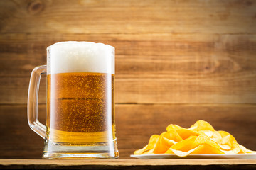 Glass with beer and chips on the background of a wooden wall.