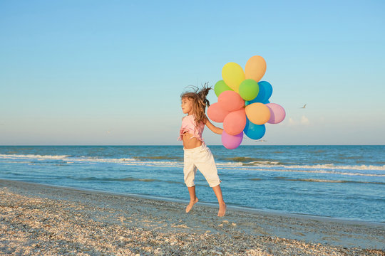 Happy little Girl on the beach with balloons.