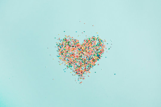Colorful heart symbol made of confetti on blue background. Flat lay, top view.