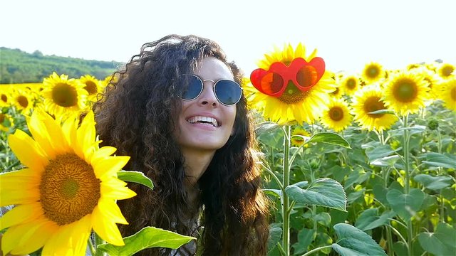 Beautiful happy girl woman smiling at sunflower with funny sunglasses on sunflower field in sunset. Slow motion
