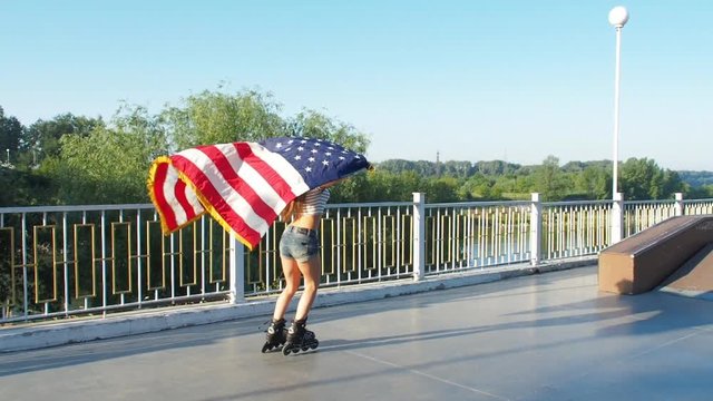 The girl skates on roller skates with the US flag. Girl teenager with the flag of the usa.