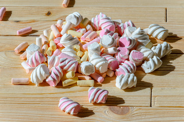 Multicolored marshmallows on bright wooden table. Background of multi-colored and different in shape and size of marshmallows. Sweets background