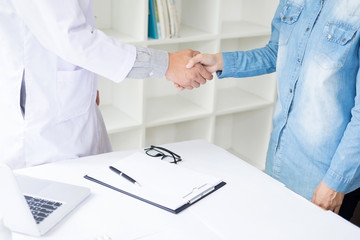 Doctor shakes hands at medical office with patient, wearing glasses, stethoscope and lab coat.