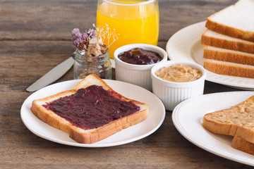 Toast bread with homemade strawberry jam and peanut butter served with orange juice. Homemade toast bread with jam and peanut butter on wood table for breakfast. Delicious toast bread ready to served.