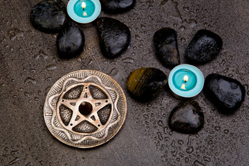 Turquoise candles with black rocks and silver pentagram on gray slate background with water droplets