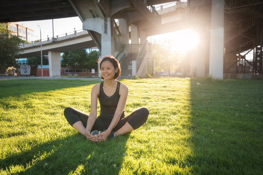 A woman stretches on the grass of a city park.