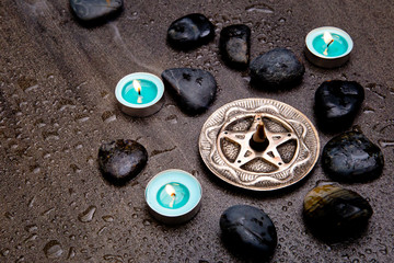 Incense burning in silver pentagram with blue candles and black rocks on gray slate stone background
