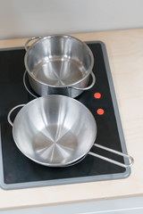 Mini stainless steel pot and pan on black electric stove over wooden countertop.