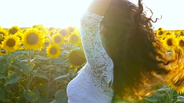 Beautiful happy girl woman playing with her curly hair at sunflower field in sunset. Slow motion