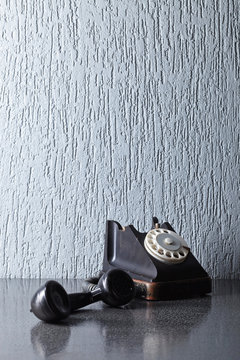 Old black phone on a grey table.