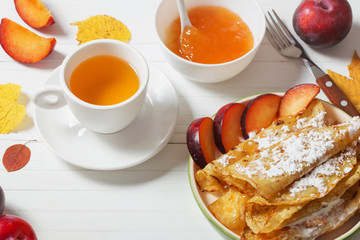 pancakes with tea  and plums on white wooden table