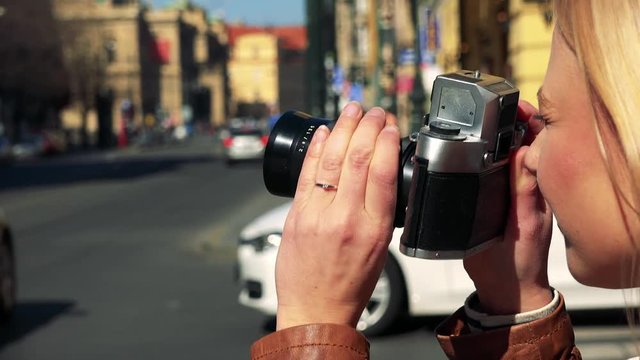 A young attractive woman takes photos with a camera in a street in an urban area - face closeup from the side