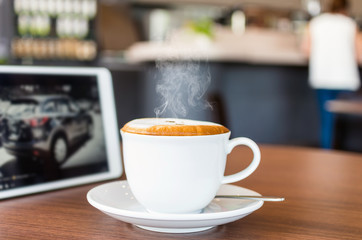 Hot Cappuccino Coffee cup with tablet on the wood table in shop