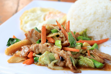 Delicious Thai dish chicken with stir fried vegetables in white dish with rice and fried egg on wooden table. Thai food.