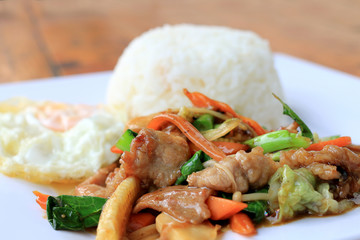 Delicious Thai dish chicken with stir fried vegetables in white dish with rice and fried egg on wooden table. Thai food.