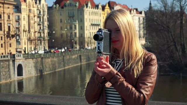A young attractive woman shoots a video with a camera - closeup - a river and a street of a quaint town in the blurry background