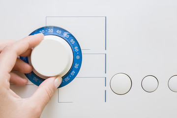 Fototapeta premium Woman's fingers turning the temperature button on the washing machine. Preparing washing a clothes.